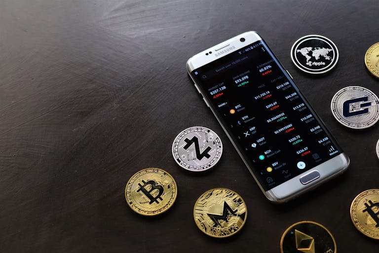 A collection of cryptocurrency coins and a smartphone displaying a digital trading platform.