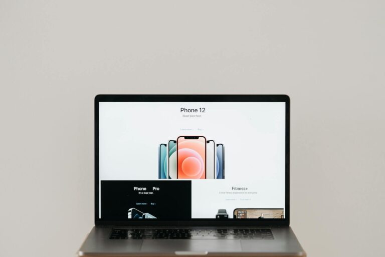 Laptop on stool showing sleek iPhone 12 ad, white background.