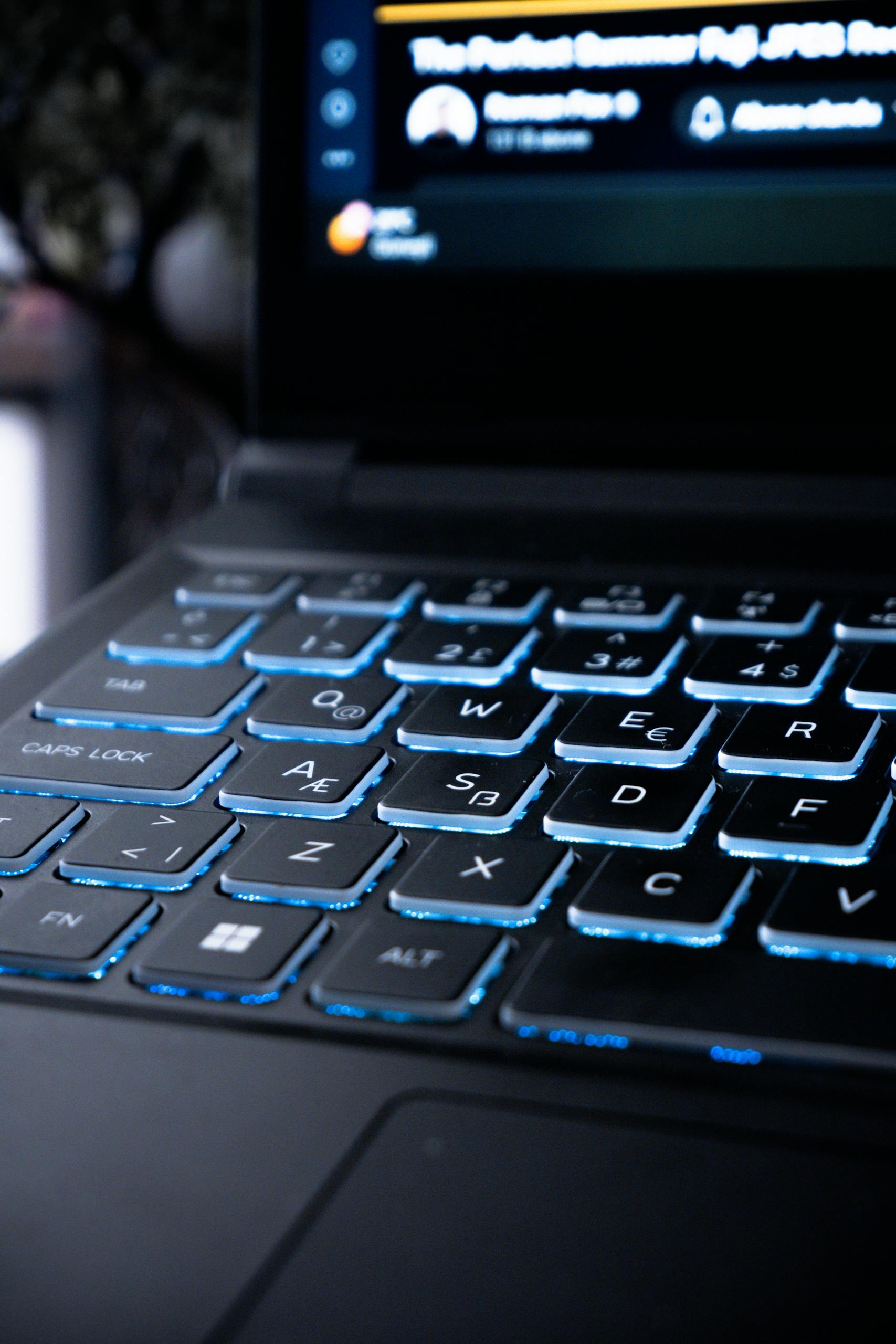 Close-up of a modern gaming laptop keyboard with blue backlit keys, suitable for tech and lifestyle themes.